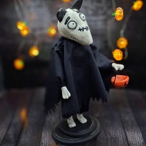 Handmade Sparky Art Doll wearing a black hoodie Halloween-style outfit, holding a pumpkin-shaped trick-or-treat box. Shown from a right diagonal angle. Whimsical and spooky Halloween home decor, unique collectible dog doll