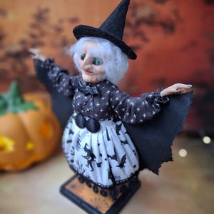 Top-left angled view of the handmade witch art doll, showcasing her witch-themed Halloween outfit, hand-painted face, and fully spread bat wings.