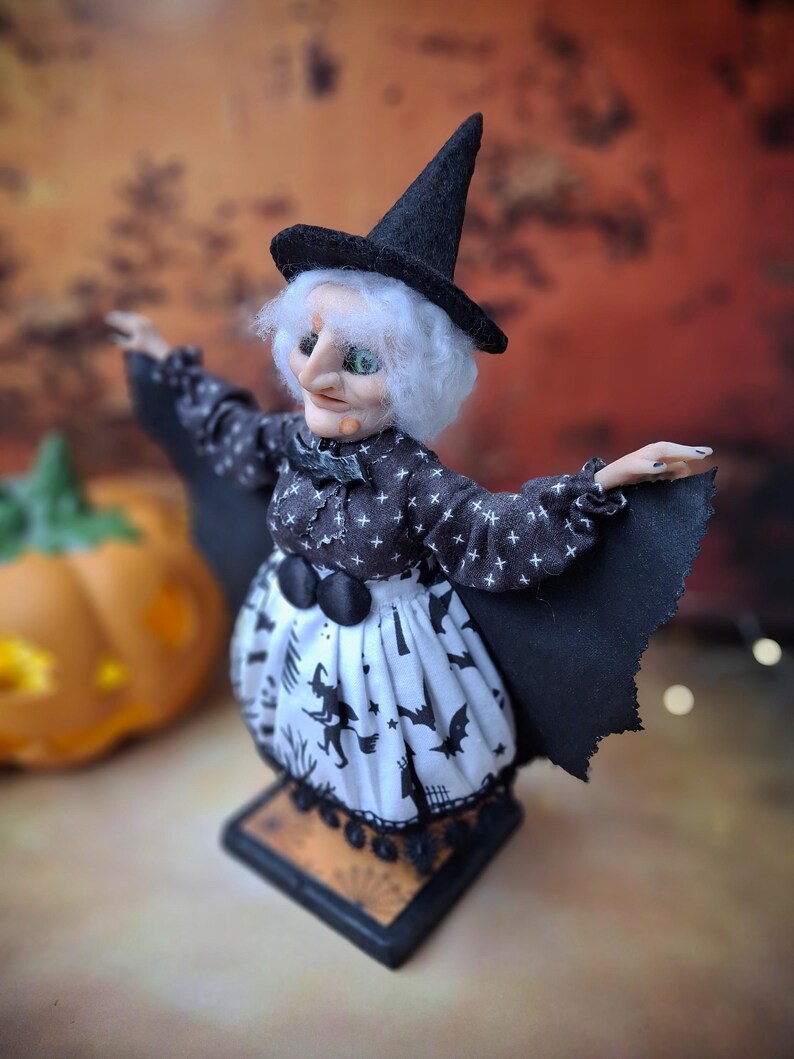 Top-left angled view of the handmade witch art doll, showcasing her witch-themed Halloween outfit, hand-painted face, and fully spread bat wings.