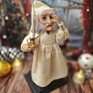 A wide right-angled view of the Ebenezer Scrooge Art Doll, with one hand resting near his face. The detailed hand-painted features, textured vintage-inspired outfit, and subtle festive accents are clearly visible, highlighting the doll’s storybook charm and whimsical holiday character.