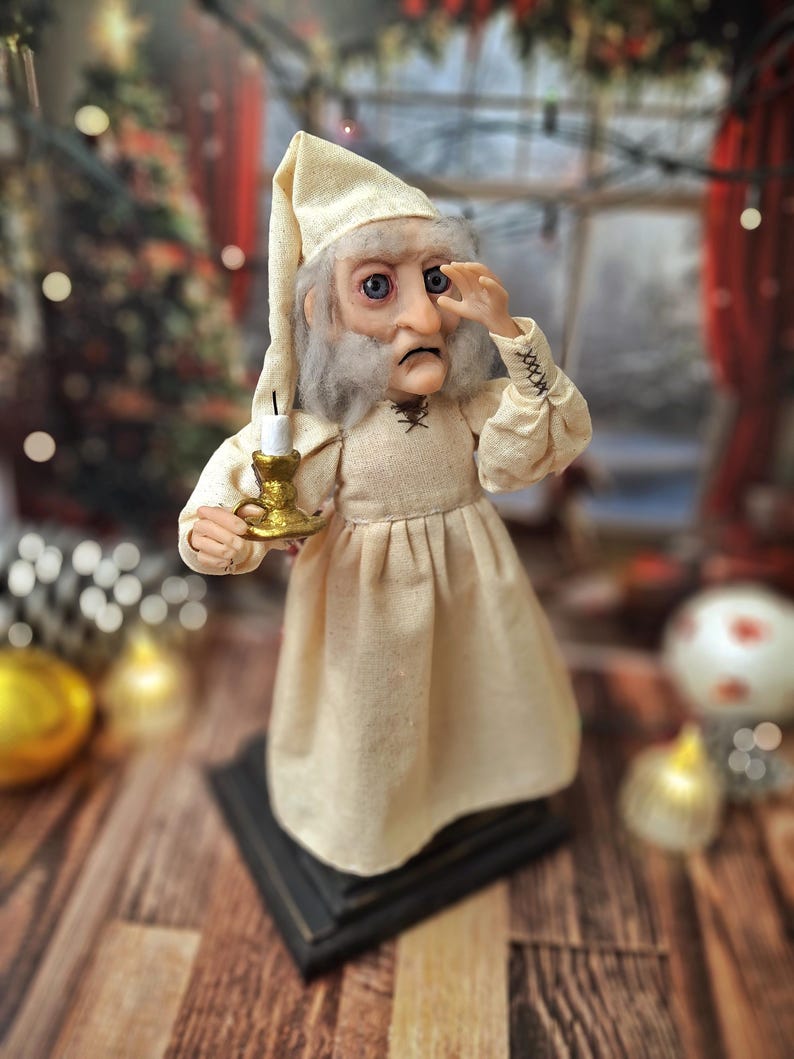 A wide right-angled view of the Ebenezer Scrooge Art Doll, with one hand resting near his face. The detailed hand-painted features, textured vintage-inspired outfit, and subtle festive accents are clearly visible, highlighting the doll’s storybook charm and whimsical holiday character.
