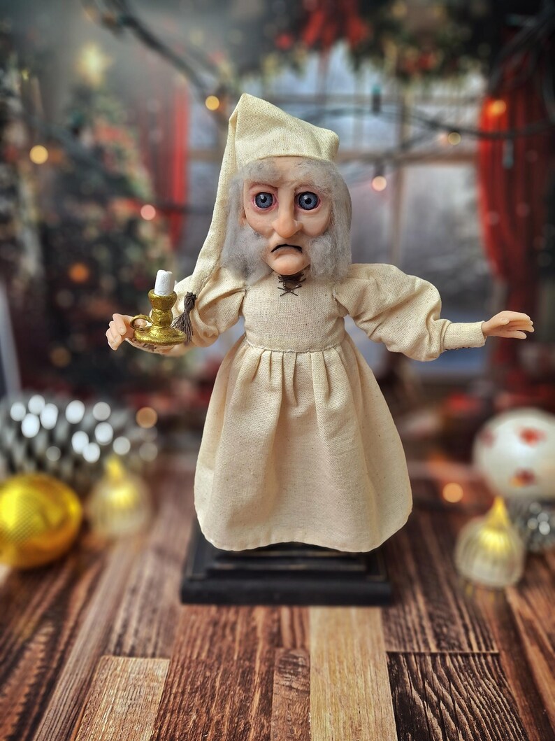 A wide front view of the Ebenezer Scrooge Art Doll, showing him with one hand raised while looking downward. The hand-painted facial expression, textured vintage-inspired outfit, and subtle holiday accents are fully visible, capturing the whimsical and classic charm of the character.