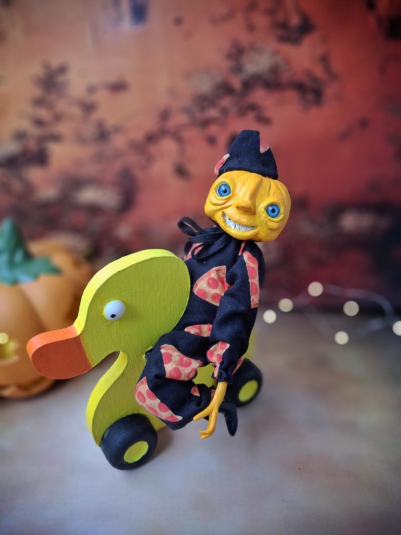 Distant left angled view of the handmade art doll, arms outstretched while playfully pushing a wooden wheeled duck toy, showing her full whimsical outfit and playful pose.