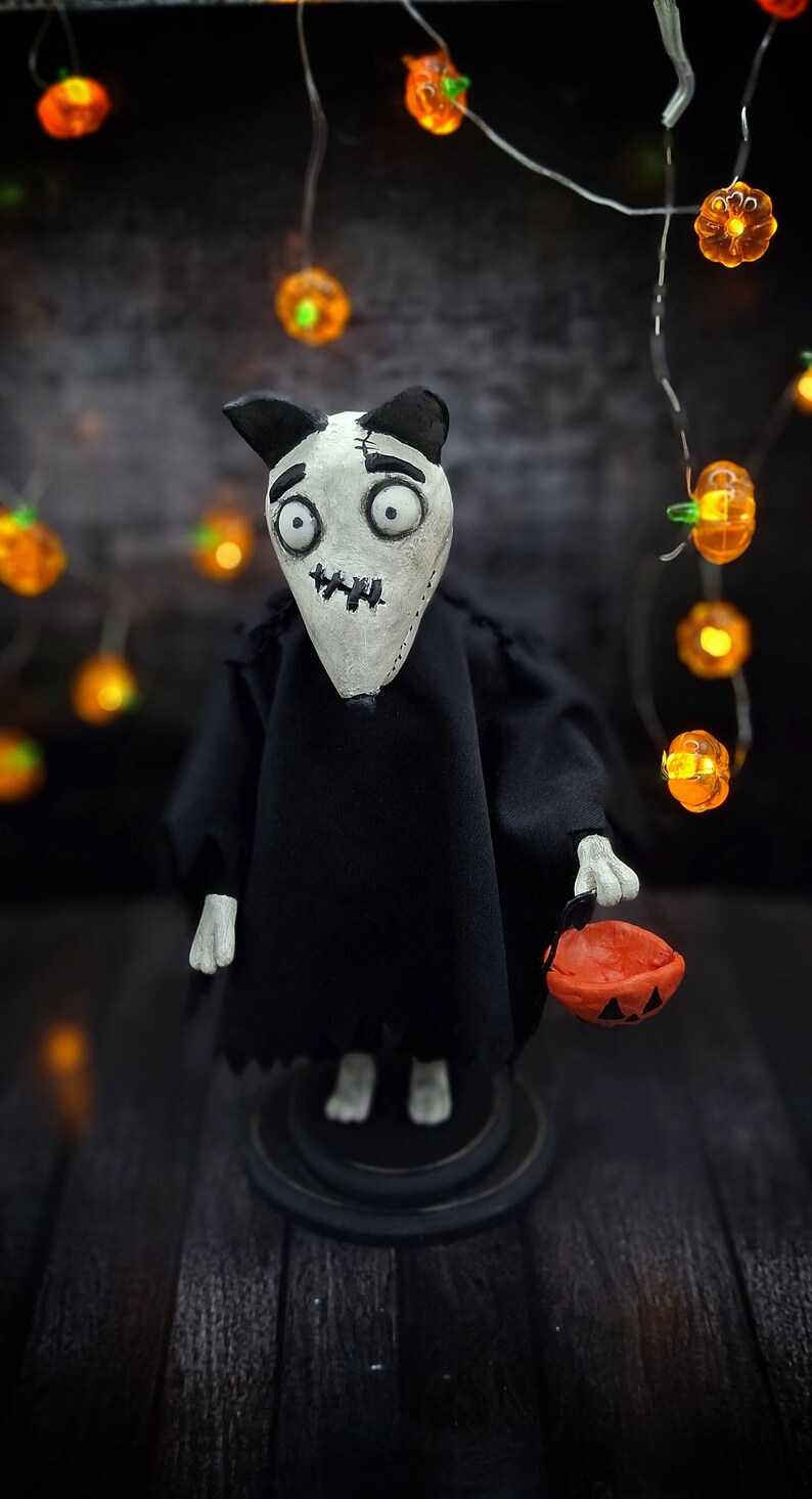Handmade Sparky Art Doll wearing a black hoodie Halloween-style outfit, holding a pumpkin-shaped trick-or-treat box. Standing straight, looking down and to the left. Whimsical and spooky Halloween home decor, unique collectible dog doll