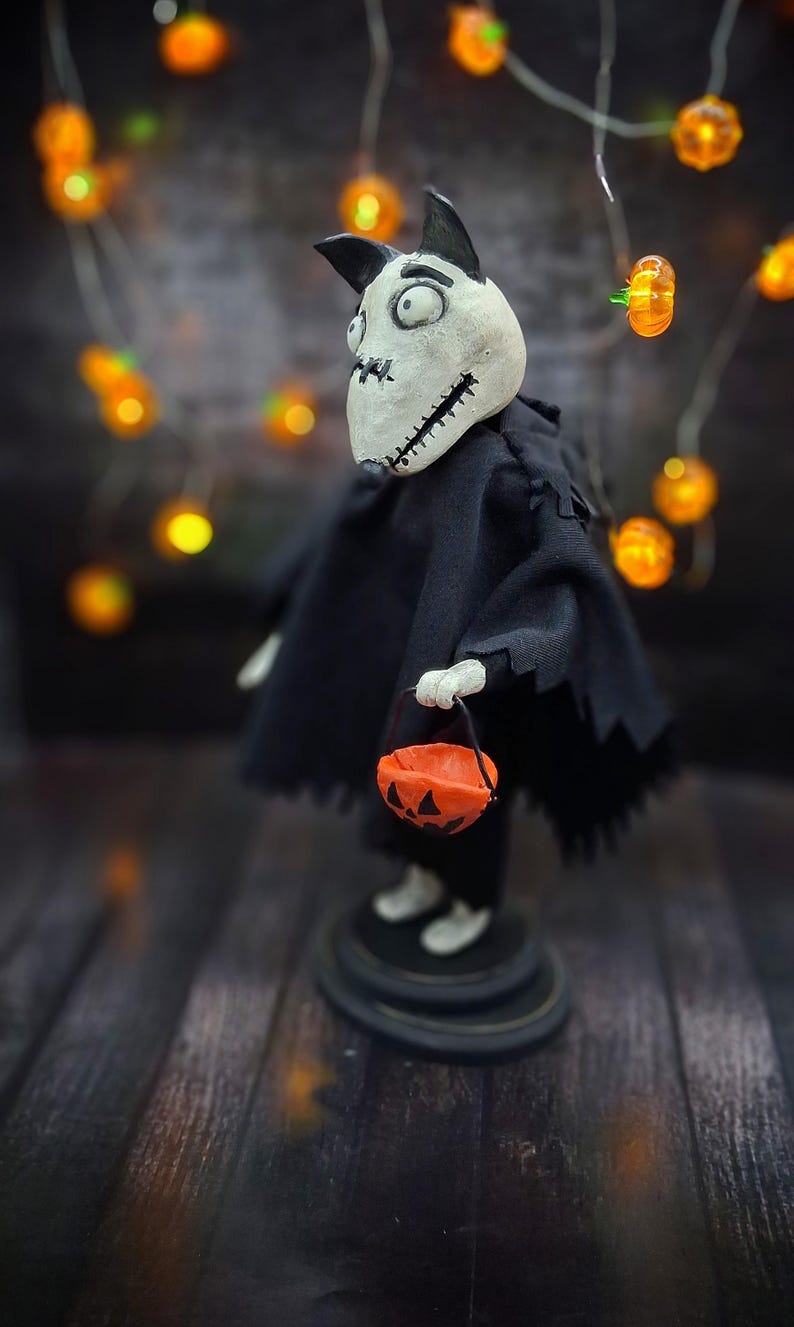 Handmade Sparky Art Doll wearing a black hoodie Halloween-style outfit, holding a pumpkin-shaped trick-or-treat box. Shown from the right profile. Whimsical and spooky Halloween home decor, unique collectible dog doll