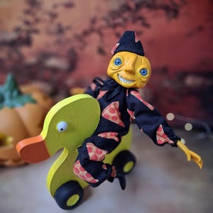 Left angled view of the handmade art doll, playfully pushing a wooden wheeled duck toy with arms outstretched, wearing a whimsical outfit.
