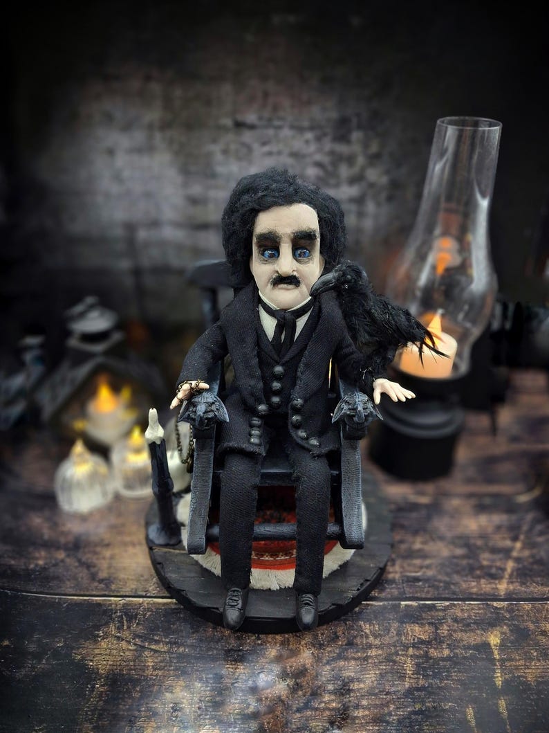 Front view of a handmade Edgar Allan Poe art doll sitting on a rocking chair on a small carpeted stand, with a raven perched nearby, a poseable art doll and unique Poe collectible perfect for literary decor, gothic home accent, and dark fantasy displays.