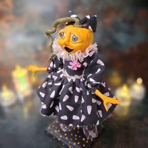 Top-left angled view of the handmade spooky Halloween pumpkin art doll, showing her pumpkin-inspired outfit, hand-painted face, and seasonal Halloween details.