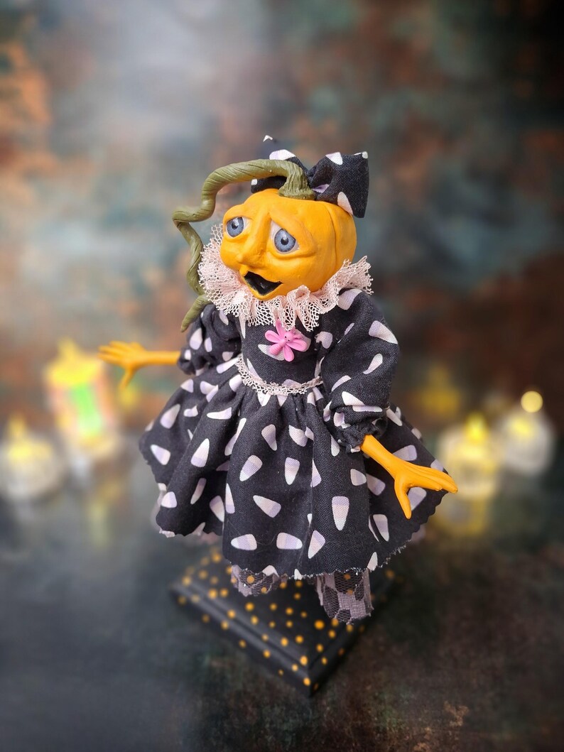 Top-left angled view of the handmade spooky Halloween pumpkin art doll, showing her pumpkin-inspired outfit, hand-painted face, and seasonal Halloween details.
