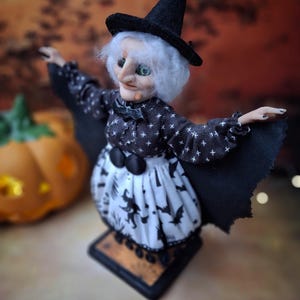 Close-up top-left angled view of the handmade witch art doll, highlighting her detailed hand-painted face, witch-themed Halloween outfit, and fully spread bat wings.
