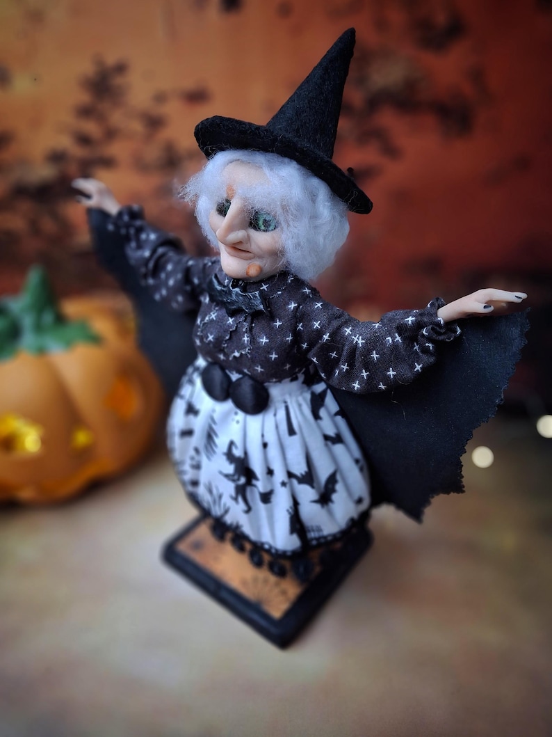 Close-up top-left angled view of the handmade witch art doll, highlighting her detailed hand-painted face, witch-themed Halloween outfit, and fully spread bat wings.
