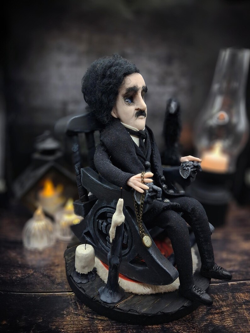 Profile view from the right of a handmade Edgar Allan Poe art doll sitting on a rocking chair on a small carpeted stand, with a raven perched nearby, a poseable art doll and unique Poe collectible perfect for literary decor, gothic home accent, and dark fantasy displays, showing detailed sculpting and painted features.