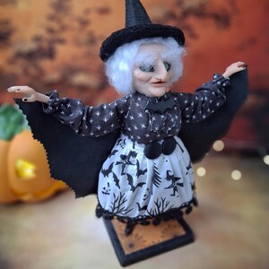 Right angled side view of the handmade witch art doll, showing her witch-themed Halloween outfit, hand-painted face, and fully spread bat wings.