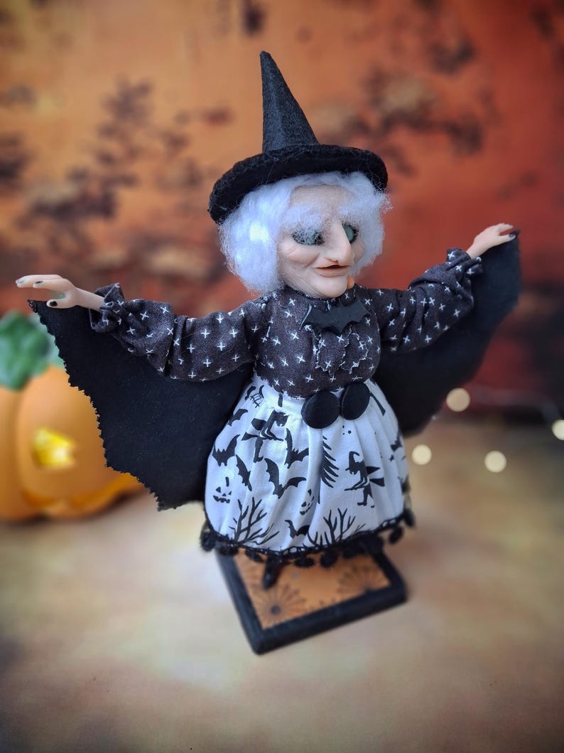Right angled side view of the handmade witch art doll, showing her witch-themed Halloween outfit, hand-painted face, and fully spread bat wings.