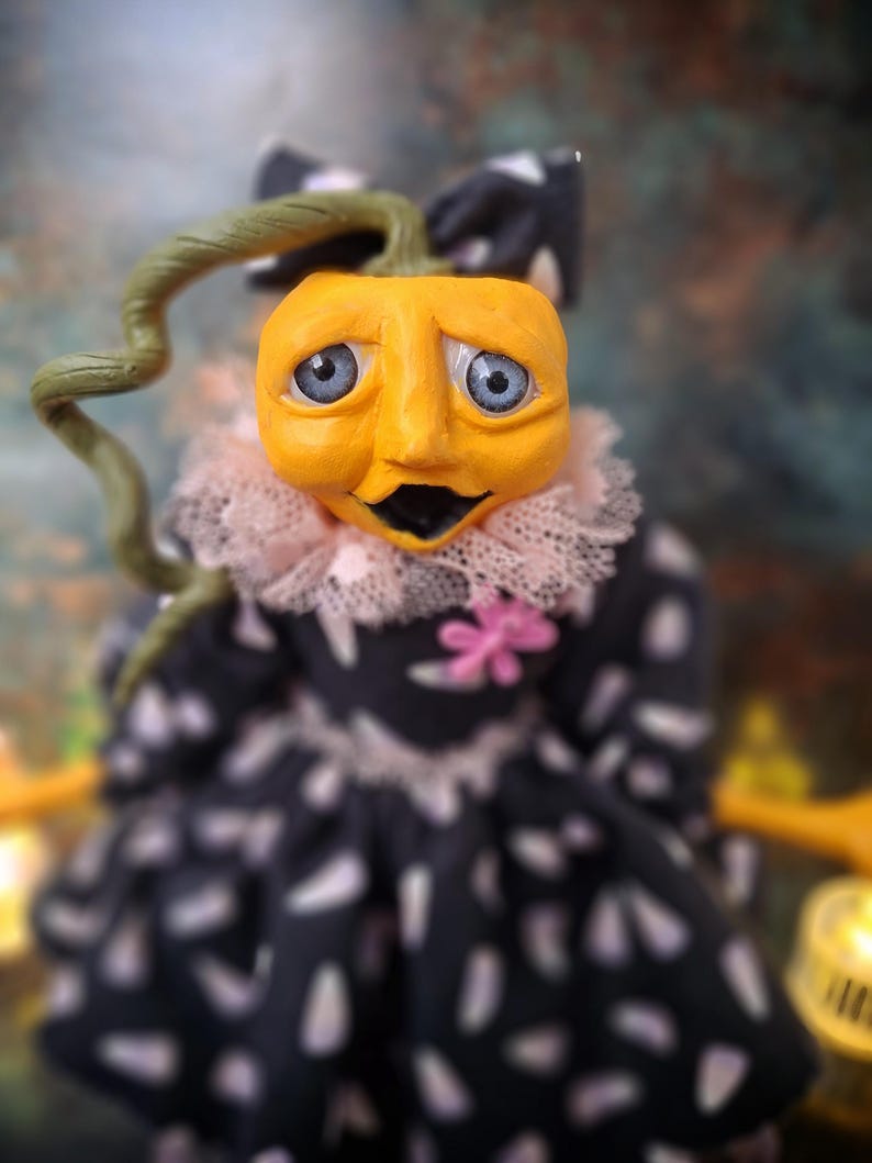 Close-up front view of the handmade spooky Halloween pumpkin art doll, focusing on her detailed hand-painted face and pumpkin-inspired outfit.