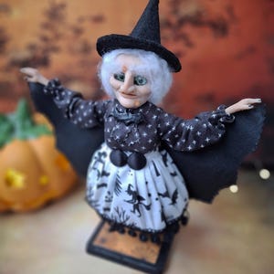 Top-left angled view of the handmade witch art doll, featuring her detailed hand-painted face, witch-themed Halloween outfit, and fully spread bat wings in a spooky pose.