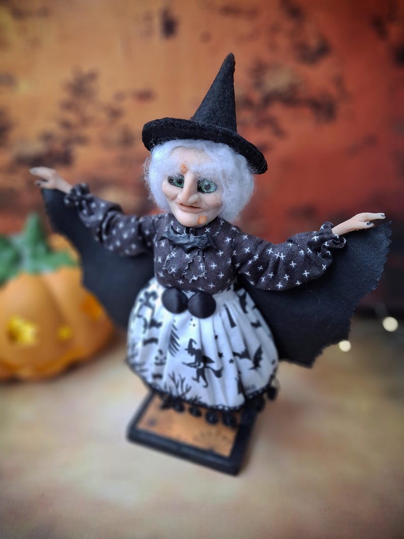 Top-left angled view of the handmade witch art doll, featuring her detailed hand-painted face, witch-themed Halloween outfit, and fully spread bat wings in a spooky pose.