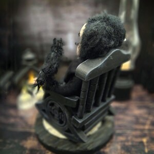 Rear-left diagonal view of a handmade Edgar Allan Poe art doll sitting on a rocking chair on a small carpeted stand, with a raven perched nearby, a poseable art doll and unique Poe collectible perfect for literary decor, gothic home accent, and dark fantasy displays, showing detailed sculpting and painted features.