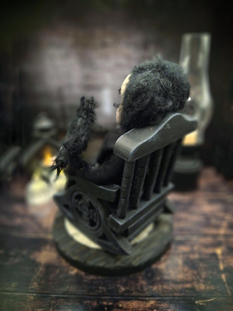 Rear-left diagonal view of a handmade Edgar Allan Poe art doll sitting on a rocking chair on a small carpeted stand, with a raven perched nearby, a poseable art doll and unique Poe collectible perfect for literary decor, gothic home accent, and dark fantasy displays, showing detailed sculpting and painted features.