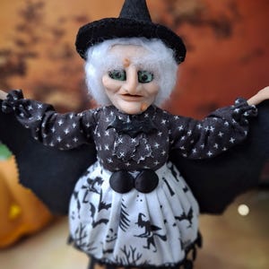 Close-up front view of the handmade witch art doll, showing detailed hand-painted face, witch-themed Halloween outfit, and fully spread bat wings.