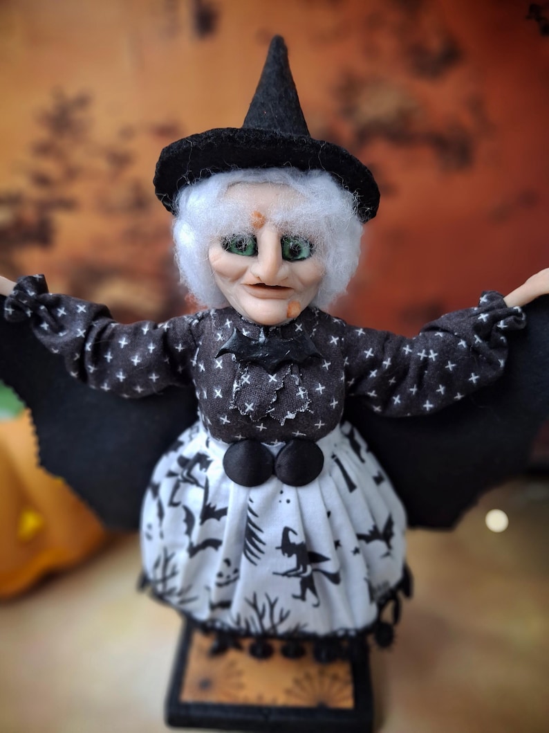 Close-up front view of the handmade witch art doll, showing detailed hand-painted face, witch-themed Halloween outfit, and fully spread bat wings.