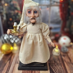 A close-up front view of the Ebenezer Scrooge Art Doll, highlighting his expressive hand-painted face, detailed outfit, and subtle festive accents. The intricate textures and whimsical storybook charm are clearly visible.