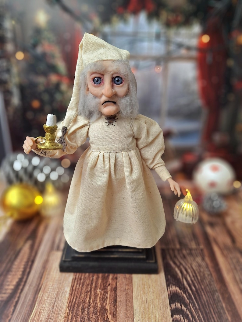 A close-up front view of the Ebenezer Scrooge Art Doll, highlighting his expressive hand-painted face, detailed outfit, and subtle festive accents. The intricate textures and whimsical storybook charm are clearly visible.