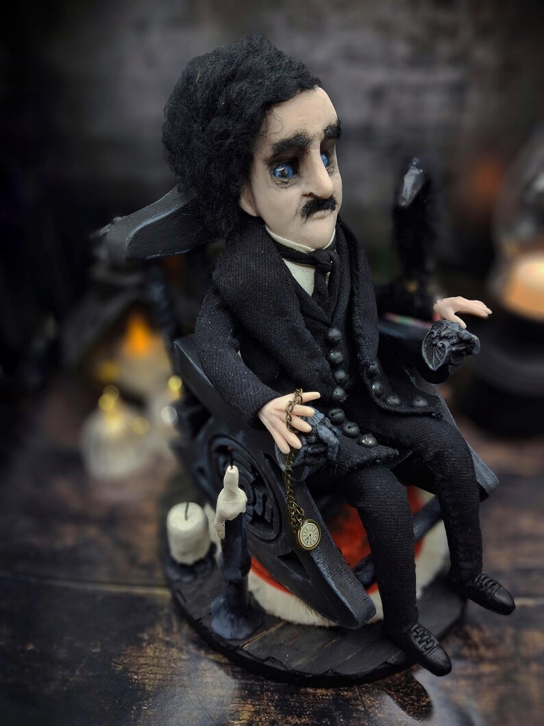 Top-down view from the right of a handmade Edgar Allan Poe art doll sitting on a rocking chair on a small carpeted stand, with a raven nearby, a poseable art doll and unique Poe collectible perfect for literary decor, gothic home accent, and dark fantasy displays, highlighting detailed sculpting and painted features.