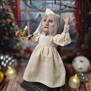 A left-angled view of the Ebenezer Scrooge Art Doll looking slightly upward, showcasing the intricate details of his hand-painted face and vintage-inspired outfit. The mixed-media textures and subtle holiday accents highlight the whimsical, storybook charm of the character.