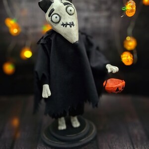 Handmade Sparky Art Doll wearing a black hoodie Halloween-style outfit, holding a pumpkin-shaped trick-or-treat box. Shown from a right diagonal angle, looking forward. Whimsical and spooky Halloween home decor, unique collectible dog doll