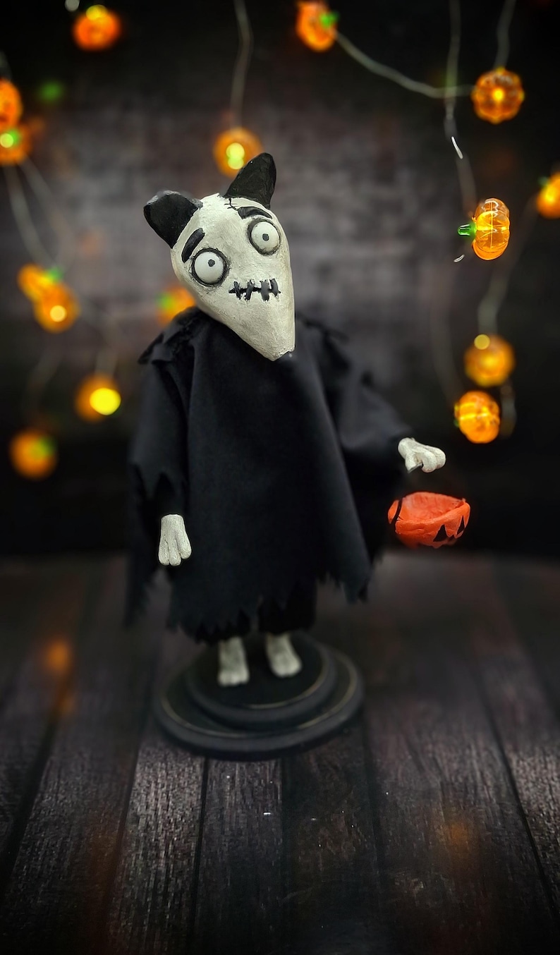 Handmade Sparky Art Doll wearing a black hoodie Halloween-style outfit, holding a pumpkin-shaped trick-or-treat box. Shown from a right diagonal angle, looking forward. Whimsical and spooky Halloween home decor, unique collectible dog doll