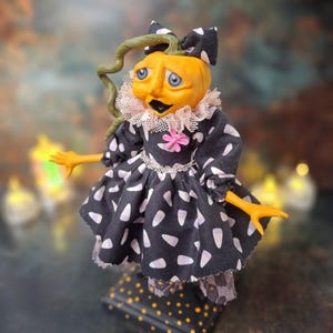 Left angled side view of the handmade spooky Halloween pumpkin art doll, showing her pumpkin-inspired outfit, hand-painted face, and festive Halloween details.