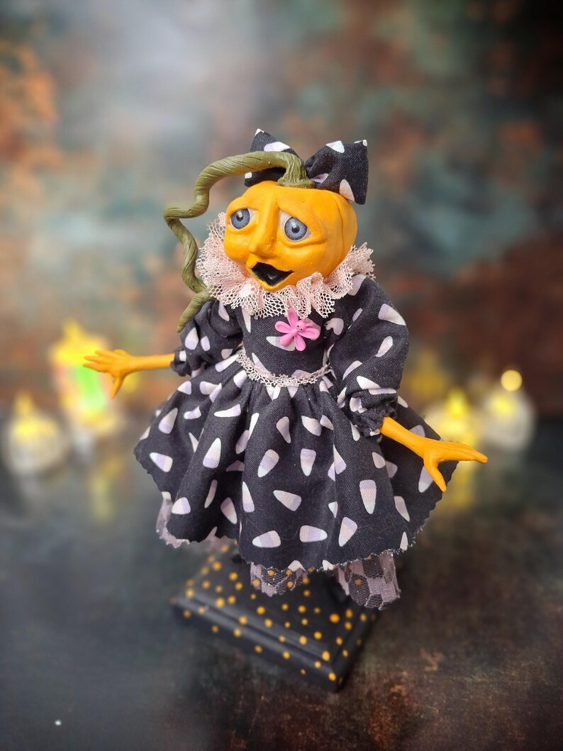 Left angled side view of the handmade spooky Halloween pumpkin art doll, showing her pumpkin-inspired outfit, hand-painted face, and festive Halloween details.