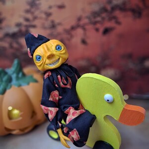 Right angled view of the handmade art doll, standing with arms lowered, looking toward the camera while pushing a wooden wheeled duck toy, wearing a whimsical outfit.