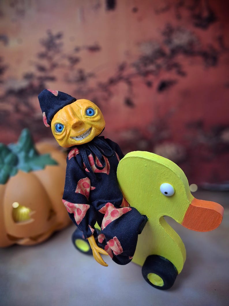 Right angled view of the handmade art doll, standing with arms lowered, looking toward the camera while pushing a wooden wheeled duck toy, wearing a whimsical outfit.