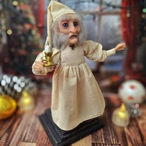 A wide right-angled view of the Ebenezer Scrooge Art Doll with one hand extended outward. The hand-painted facial features, detailed vintage-inspired outfit, and subtle festive accents are visible, capturing the whimsical and classic holiday charm of the character.