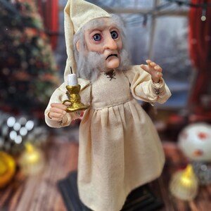 A close-up right-angled view of the Ebenezer Scrooge Art Doll, highlighting the detailed hand-painted features, expressive face, and textured outfit. The subtle festive accents and vintage-inspired craftsmanship are clearly visible, capturing the doll’s storybook charm.