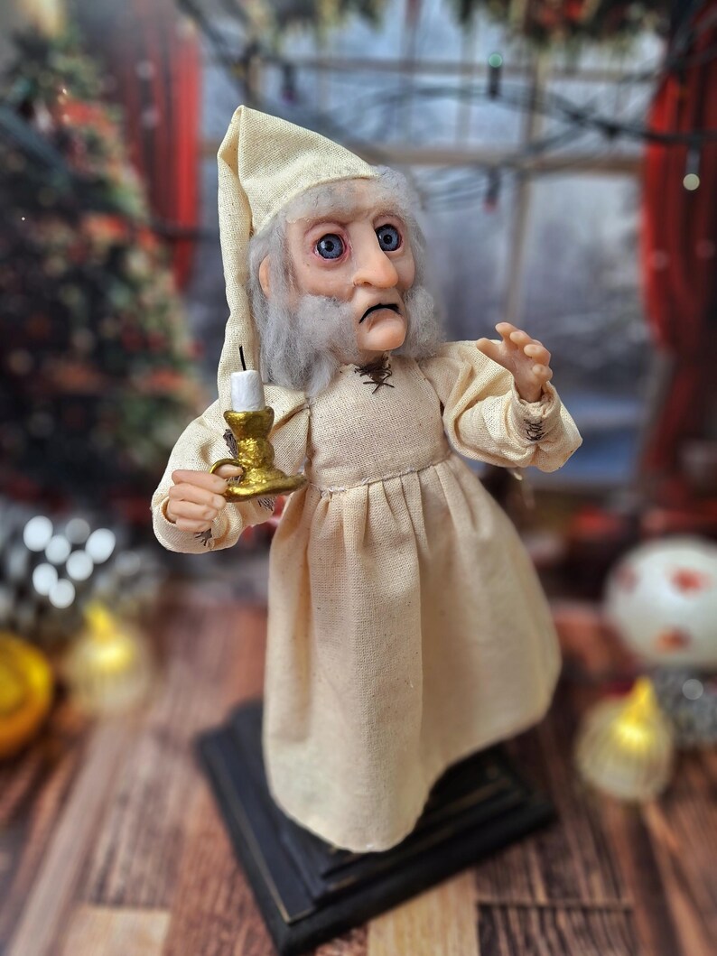 A close-up right-angled view of the Ebenezer Scrooge Art Doll, highlighting the detailed hand-painted features, expressive face, and textured outfit. The subtle festive accents and vintage-inspired craftsmanship are clearly visible, capturing the doll’s storybook charm.