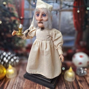 A left-side profile view of the Ebenezer Scrooge Art Doll, showcasing the detailed hand-painted facial features and the textured vintage-inspired outfit. The mixed-media elements and subtle holiday accents highlight the doll’s whimsical, storybook charm.