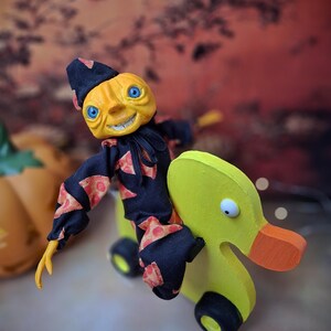 Side view from the right of the handmade art doll, arms outstretched while playfully pushing a wooden wheeled duck toy, showing her whimsical outfit and hand-painted details.
