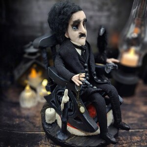 Mid-angle view from the right of a handmade Edgar Allan Poe art doll sitting on a rocking chair on a small carpeted stand, with a raven perched nearby, a poseable art doll and unique Poe collectible perfect for literary decor, gothic home accent, and dark fantasy displays, highlighting detailed sculpting and painted features.