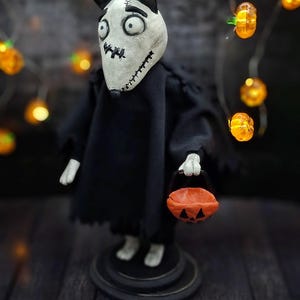 Handmade Sparky Art Doll wearing a black hoodie Halloween-style outfit, holding a pumpkin-shaped trick-or-treat box. Shown from a right diagonal angle, looking downward. Whimsical and spooky Halloween home decor, unique collectible dog doll