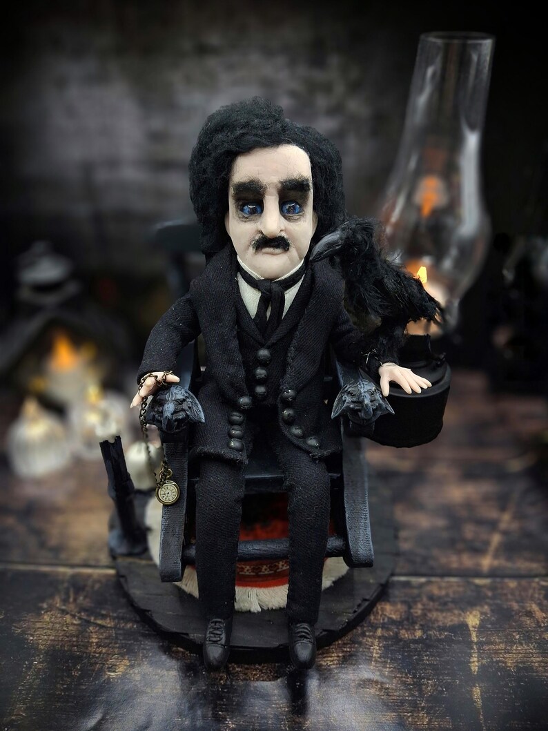 Handmade Edgar Allan Poe art doll sitting slightly tilted to the left on a rocking chair on a small carpeted stand, with a raven perched nearby, a poseable art doll and unique Poe collectible perfect for literary decor, gothic home accent, and dark fantasy displays, highlighting detailed sculpting and painted features.