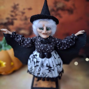 Close-up front view of the handmade witch art doll, highlighting her detailed hand-painted face, witch-themed Halloween outfit, and fully spread bat wings.