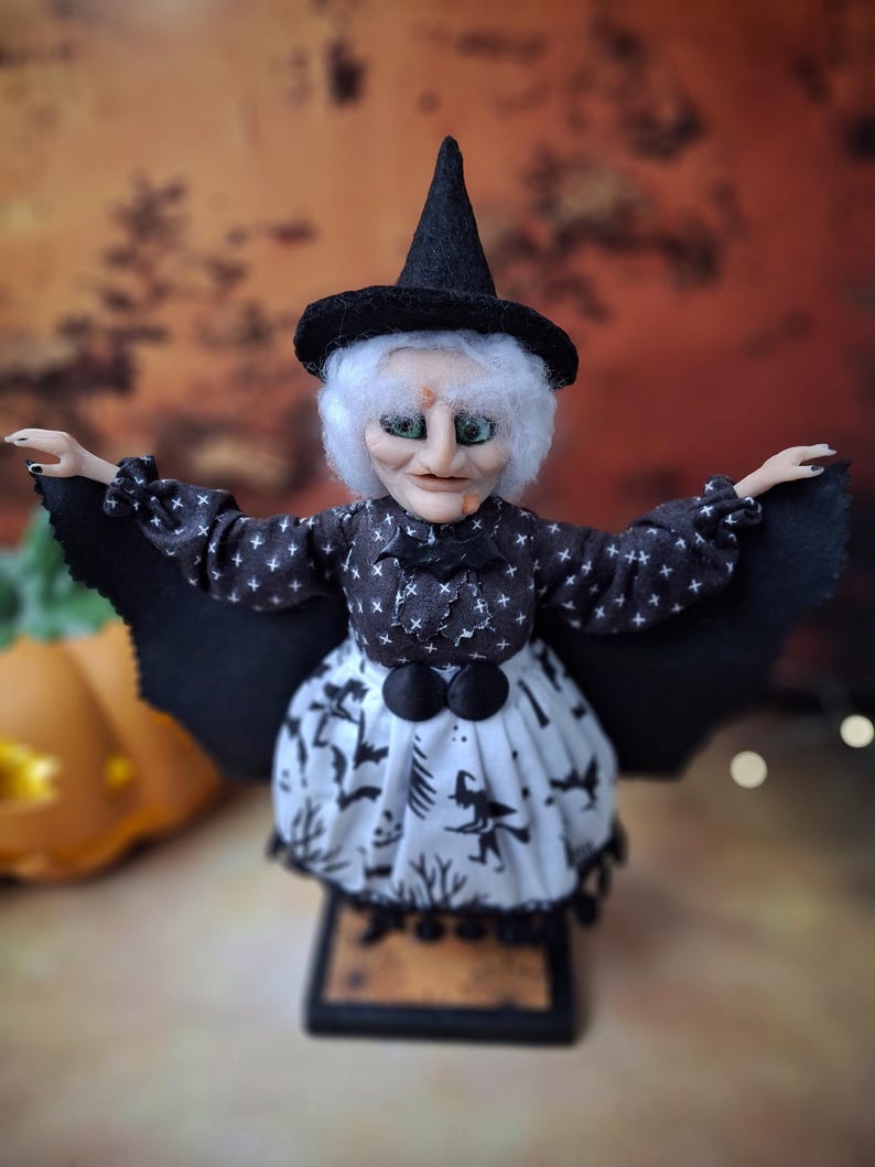 Close-up front view of the handmade witch art doll, highlighting her detailed hand-painted face, witch-themed Halloween outfit, and fully spread bat wings.
