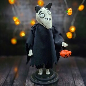 Handmade Sparky Art Doll wearing a black hoodie Halloween-style outfit, holding a pumpkin-shaped trick-or-treat box. Standing straight, looking to the right. Unique whimsical and spooky Halloween home decor collectible dog doll