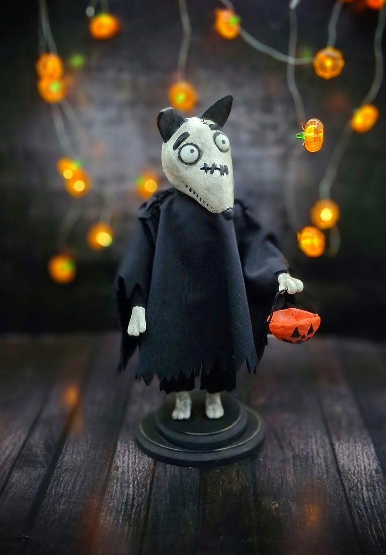 Handmade Sparky Art Doll wearing a black hoodie Halloween-style outfit, holding a pumpkin-shaped trick-or-treat box. Standing straight, looking to the right. Unique whimsical and spooky Halloween home decor collectible dog doll