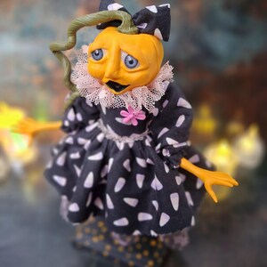 Top-down close-up view of the handmade spooky Halloween pumpkin art doll from the left side profile, showing her pumpkin-inspired outfit, hand-painted face, and festive Halloween details.