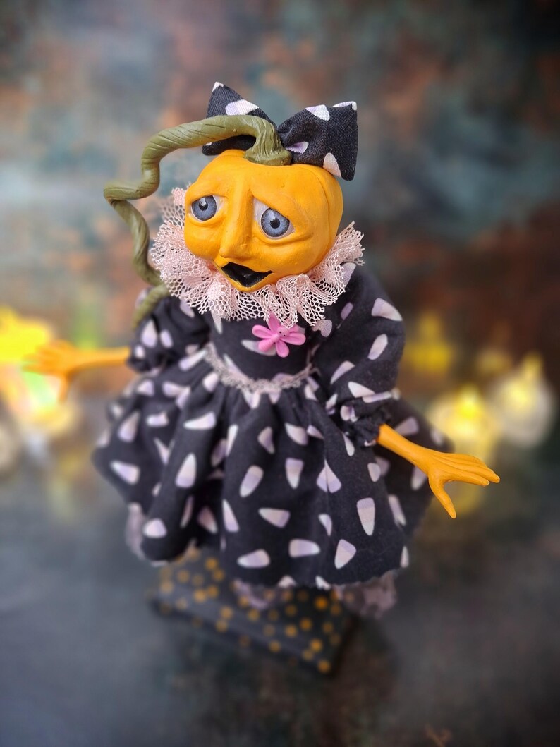 Top-down close-up view of the handmade spooky Halloween pumpkin art doll from the left side profile, showing her pumpkin-inspired outfit, hand-painted face, and festive Halloween details.