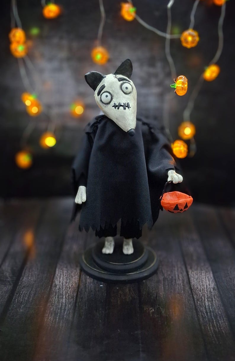 Wide shot of Handmade Sparky Art Doll wearing a black hoodie Halloween-style outfit, holding a pumpkin-shaped trick-or-treat box. Standing straight, facing slightly to the right. Unique whimsical and spooky Halloween home decor collectible dog doll